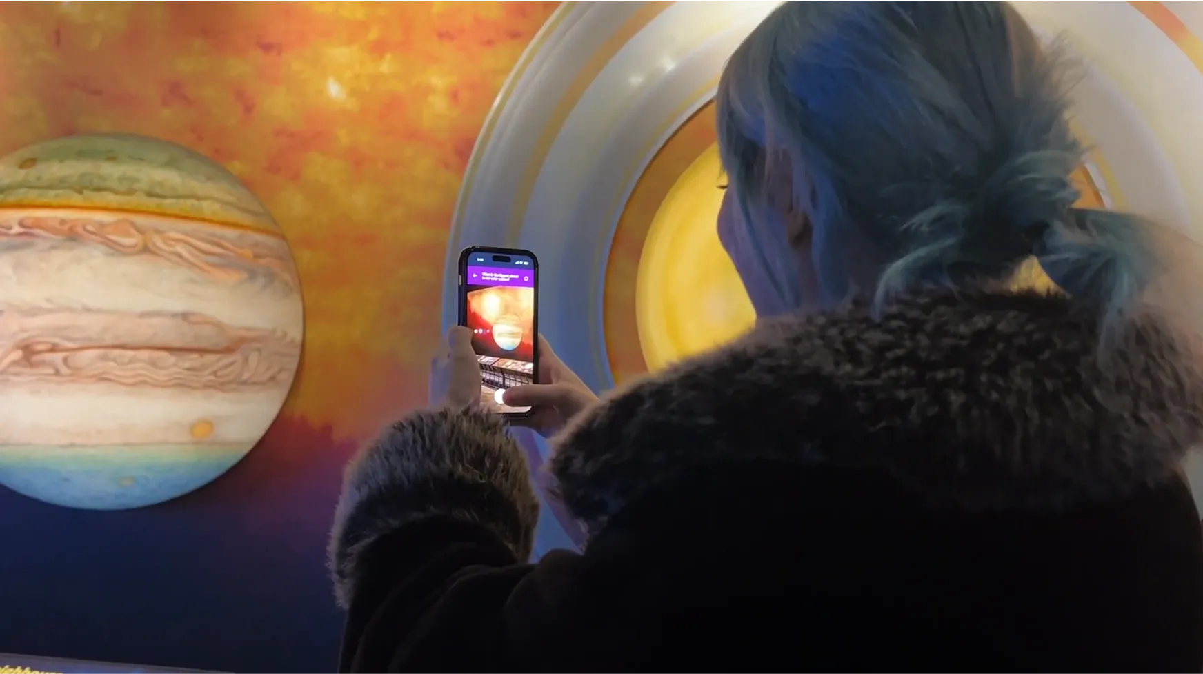 User in the Space Gallery using the AR app on their phone to scan a planet exhibit.