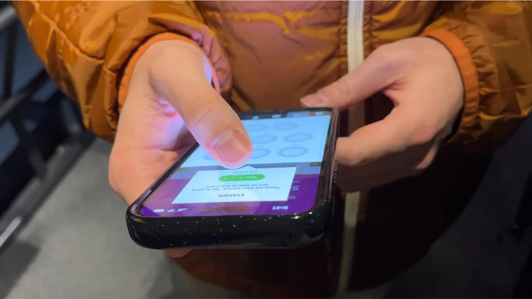 Close-up of a user’s hand tapping the app’s stamp-book interface during on-site testing.