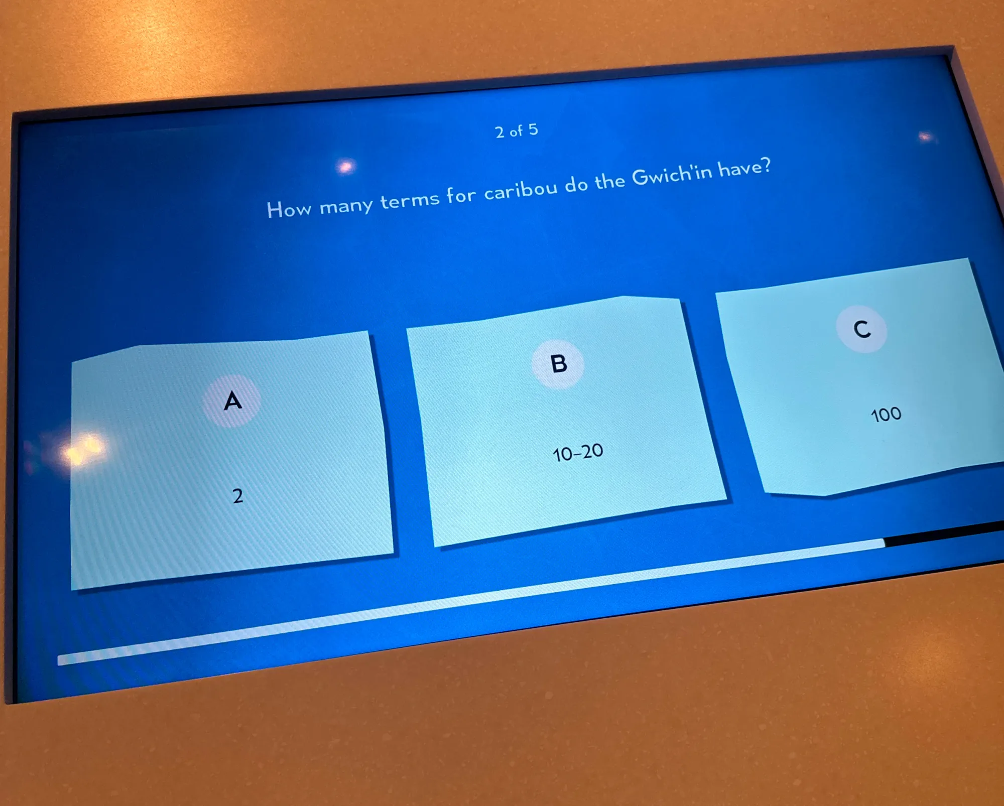 An interactive touchscreen quiz with answer cards and a progress indicator.